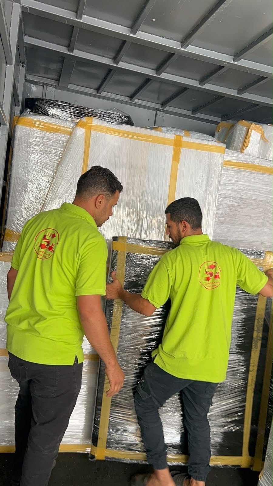 فريق المؤسسة يحمل أثاثًا مغلفًا داخل سيارة النقل